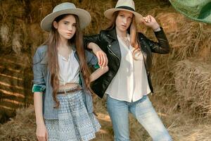 Two teenage girls posing in hayloft against background of stacks of hay photo