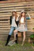 Two teenage girls wearing country style clothes standing against wooden planks wall background photo