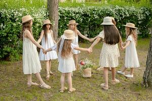 grupo de preadolescente muchachas en ligero vestidos bailando en circulo en verde verano parque foto