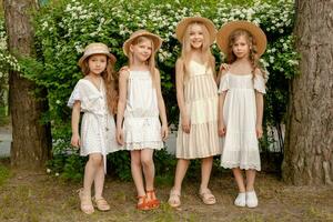 Cute preteen girls in light dresses standing near flowering bush in park photo