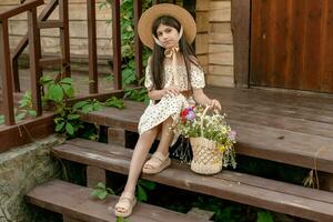 Dark-haired tween girl sitting on wooden doorstep with basket of wildflowers photo