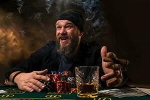 hombre es jugando póker con un cigarro y un whisky. un hombre victorioso todas el papas fritas en el mesa con grueso cigarrillo fumar. foto