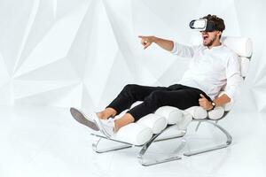 Excited young man is getting experience using VR-headset glasses of virtual reality gesticulating with his hands photo