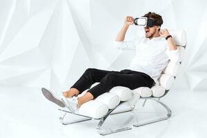 Excited young man is getting experience using VR-headset glasses of virtual reality gesticulating with his hands photo