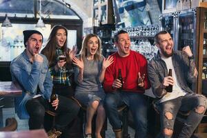 Group of young beautiful friends watching TV and cheering for th photo