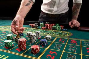 A close-up vibrant image of green casino table with roulette, with the hands of croupier and multicolored chips. photo