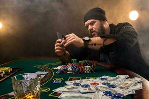 barbado hombre con cigarro y vaso sentado a póker mesa en un casino. juego, jugando tarjetas y ruleta. foto