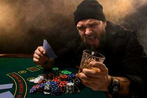 barbado hombre con cigarro y vaso sentado a póker mesa en un casino. juego, jugando tarjetas y ruleta. foto