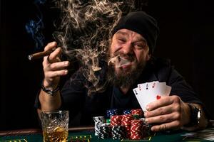 barbado hombre Bebiendo whisky y de fumar un cigarro mientras jugando póker foto
