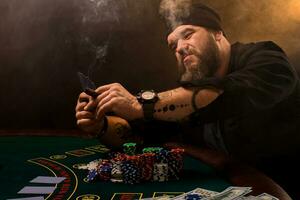 barbado hombre con cigarro y vaso sentado a póker mesa en un casino. juego, jugando tarjetas y ruleta. foto