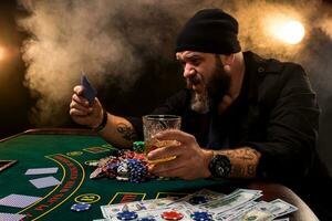 barbado hombre con cigarro y vaso sentado a póker mesa en un casino. juego, jugando tarjetas y ruleta. foto