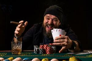 barbado hombre con cigarro y vaso sentado a póker mesa en un casino. juego, jugando tarjetas y ruleta. foto