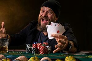 Bearded man with cigar and glass sitting at poker table and screaming isolated on black photo