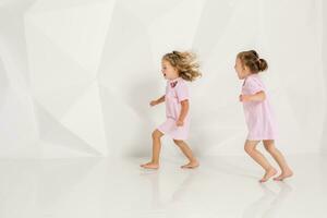 Two little funny and laughing girl in gently pink dresses playing in white studio photo