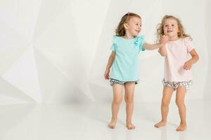 dos pequeño gracioso y riendo niña en el idéntico ropa de diferente colores jugando en blanco estudio foto