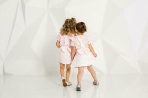 Two little funny and laughing girl in gently pink dresses playing in white studio photo