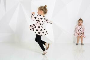 Two little funny and laughing girl in gently pink dresses playing in white studio photo