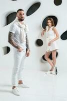 Casual couple near a white wall, man and woman in white clothing. photo
