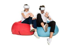 emocionado joven Pareja experimentando virtual realidad sentado en bolsas de frijol aislado en blanco antecedentes foto