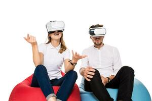 Excited young couple experiencing virtual reality seated on beanbags isolated on white background photo