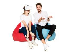 Smiling friends experiencing virtual reality glasses seated on beanbags isolated on white background. photo