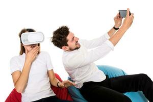 Smiling friends experiencing virtual reality glasses seated on beanbags isolated on white background. photo