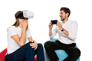 emocionado joven Pareja experimentando virtual realidad sentado en bolsas de frijol aislado en blanco antecedentes foto