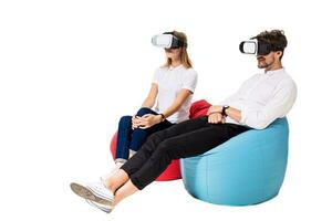 Excited young couple experiencing virtual reality seated on beanbags isolated on white background photo