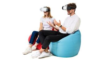 Excited young couple experiencing virtual reality seated on beanbags isolated on white background photo