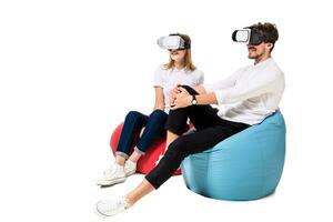 Excited young couple experiencing virtual reality seated on beanbags isolated on white background photo