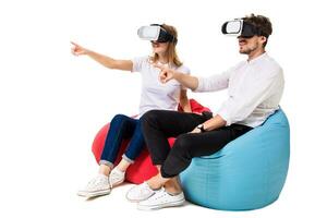 Excited young couple experiencing virtual reality seated on beanbags isolated on white background photo