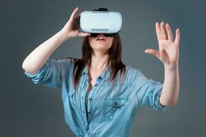 Emotional young woman using a VR headset and experiencing virtual reality on grey background photo