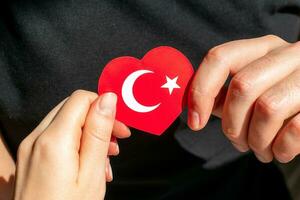 bandera de Turquía en el formar de un corazón en el manos de un hombre y un mujer en un negro antecedentes. foto