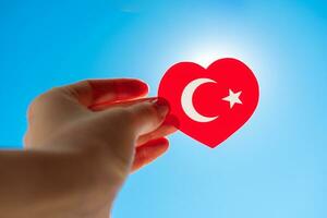 Flag of Turkey in the form of a heart in the hand of a girl against the blue sky. photo