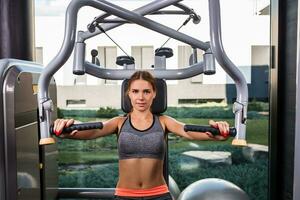 Muscular young woman doing exercises on the simulator in the gym photo