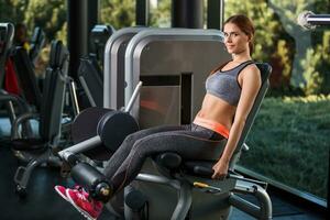 Muscular young woman doing exercises on the simulator in the gym photo