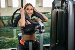 Muscular young woman doing exercises on the simulator in the gym photo