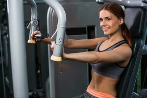 Muscular young woman doing exercises on the simulator in the gym photo