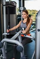 Muscular young woman doing exercises on the simulator in the gym photo