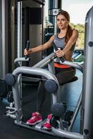 Muscular young woman doing exercises on the simulator in the gym photo