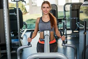 muscular joven mujer haciendo ejercicios en el simulador en el gimnasio foto