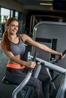 Muscular young woman doing exercises on the simulator in the gym photo