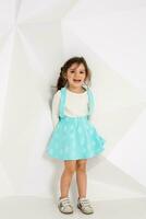 Beautiful little girl with long hair. In a lush short turquoise skirt and white T-shirt. photo