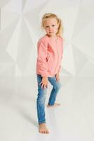 linda pequeño niña en rosado chaqueta y pantalones en blanco antecedentes foto