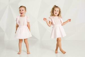 Two little funny and laughing girl in gently pink dresses posing in white studio photo