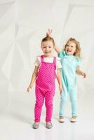 Two little girlfriends in the identical overalls of different colors in a studio with white walls photo