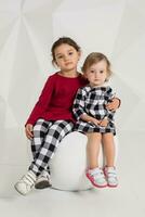 niños, dos hermanas 1,5 y 5 5 años antiguo en el disfraces de diferente colores, pequeño muchachas en un blanco antecedentes en el estudio foto
