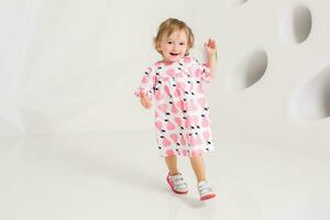 Year-old child in summer dress standing near white wall in studio photo