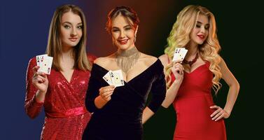 Three models in red and black dresses, stylish jewelry. They smiling, showing aces, posing against colorful background. Poker, casino. Close-up photo