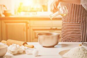 Young woman pouring oil into a bowl with dough, close-up photo